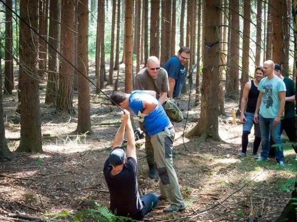 Personen arbeiten zusammen an einer selbstgebauten Seilbrücke im Wald