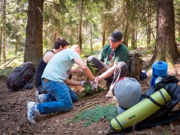 Personen bauen eine kleine Struktur aus Ästen im Wald beim Survival Training