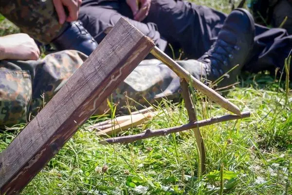 Schlagfalle (Figure-Four) aus Holzstücken im Gras aufgebaut