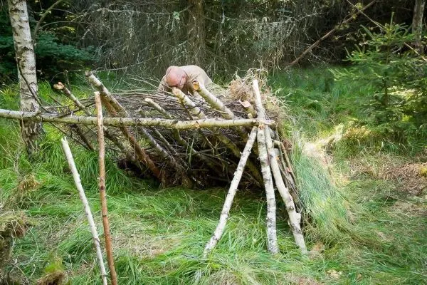 Selbstgebaute Tarp-Notunterkunft wird mit Ästen und Gras verstärkt