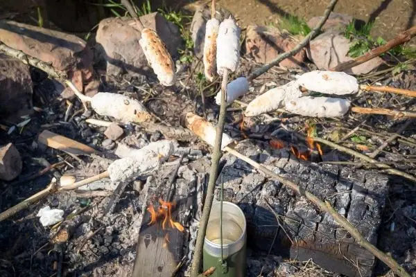 Teigstücke rösten über einem offenen Feuer auf Stockspitzen