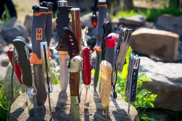 Verschiedene Messer und Multitools stecken in einem Holzblock im Freien