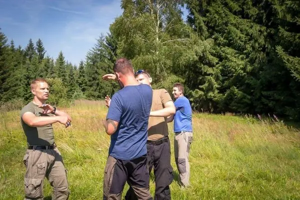 Vier Personen üben Techniken in einer Wiese umgeben von Bäumen