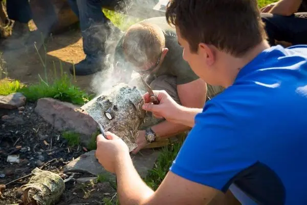 Zunder glimmt auf einem Holzstück, während ein Teilnehmer Funken erzeugt