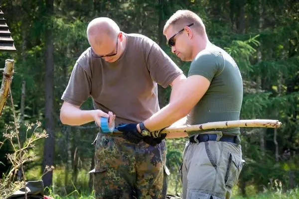 Zwei Personen befestigen mit Klebeband einen Stock im Freien
