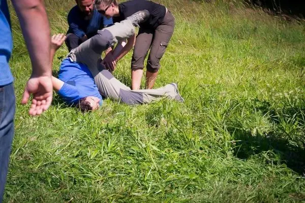 Zwei Personen helfen einem Mann, der auf dem Gras liegt und sich umdreht