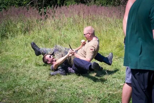 Zwei Personen im Bodenkampf auf einer Wiese, eine Person hält den Arm des anderen