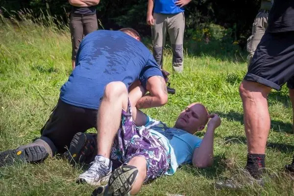 Zwei Personen im Bodenkampf auf einer Wiese, eine Person hält die andere fest
