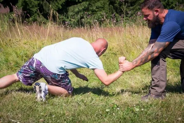Zwei Personen im Ringen auf einer Wiese, einer kniet, der andere steht