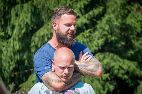 Zwei Personen üben eine Haltegriff-Technik im Freien unter Bäumen