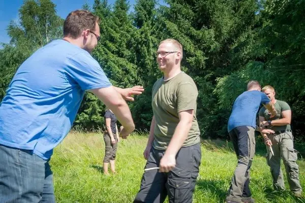 Zwei Personen üben eine Technik im Freien, umgeben von Bäumen und Gras