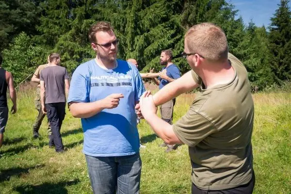 Zwei Personen üben eine Technik im Freien, umgeben von weiteren Teilnehmern