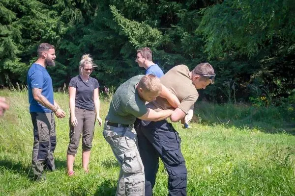Zwei Personen üben eine Technik zur Kontrolle in einer Wiese, während andere zuschauen