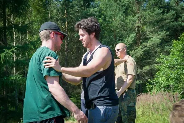 Zwei Personen umarmen sich, während eine dritte Person im Hintergrund beobachtet