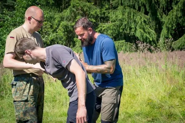 Zwei Personen unterstützen einen Dritten bei einer praktischen Übung im Freien