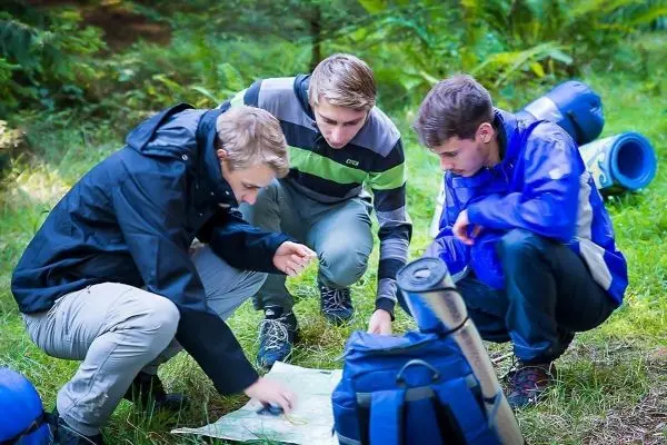 Drei Personen betrachten eine Karte auf dem Boden im Wald