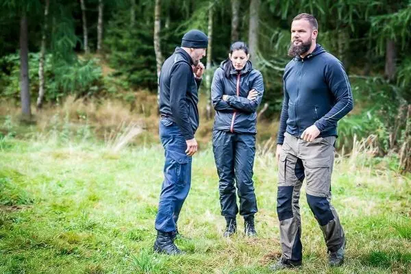 Drei Personen in Outdoor-Bekleidung stehen auf einer Wiese im Wald