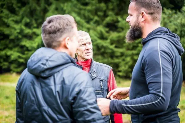 Drei Personen stehen im Gespräch, umgeben von grüner Vegetation