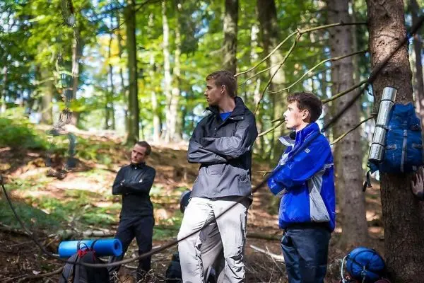 Drei Personen stehen im Wald, Rucksäcke und Ausrüstung liegen am Boden
