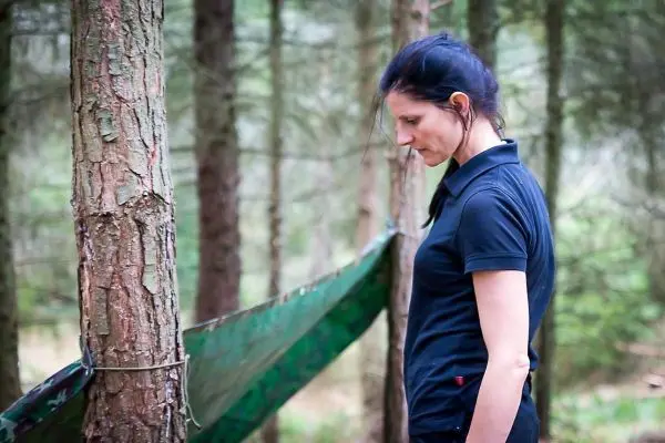 Frau steht neben einem Baum und betrachtet eine Tarp-Notunterkunft