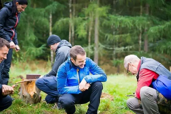 Gruppe arbeitet an Holzstücken im Wald, einige Personen sitzen und diskutieren