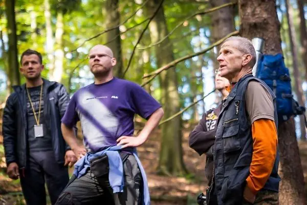 Gruppe hört einem Trainer im Wald aufmerksam zu