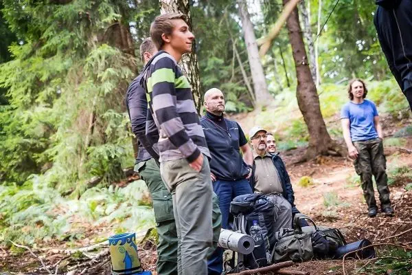 Gruppe steht im Wald neben Rucksäcken und Ausrüstung auf dem Boden