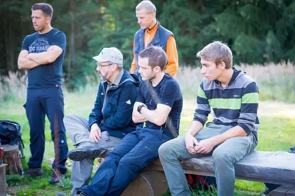 Gruppe von Personen sitzt auf einer Holzbank und hört aufmerksam zu