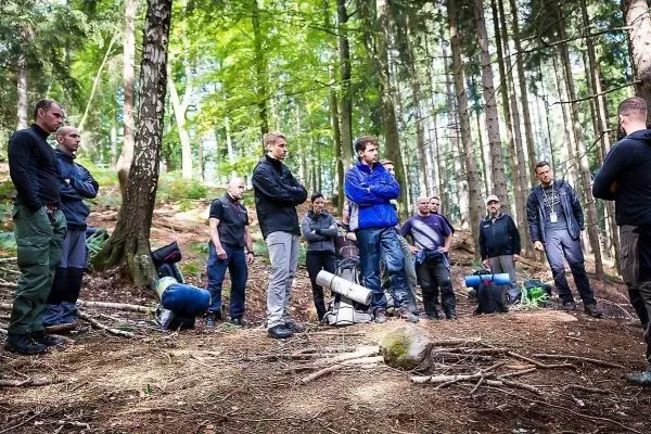 Gruppe von Personen steht im Wald, einige mit Rucksäcken, in angeregter Diskussion