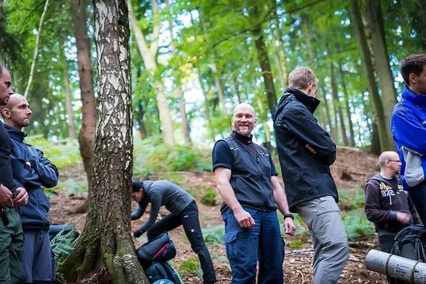 Gruppe von Personen steht im Wald, einige packen Rucksäcke aus