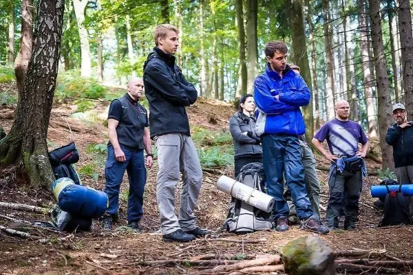 Gruppe von Personen steht im Wald, Rucksäcke liegen auf dem Boden