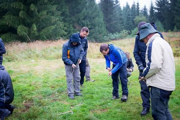 Gruppenteilnehmer bearbeiten Holzstücke auf einer Wiese im Wald