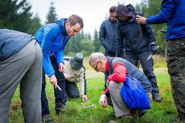 Gruppenteilnehmer untersuchen den Boden und nutzen Messer zur Materialsuche