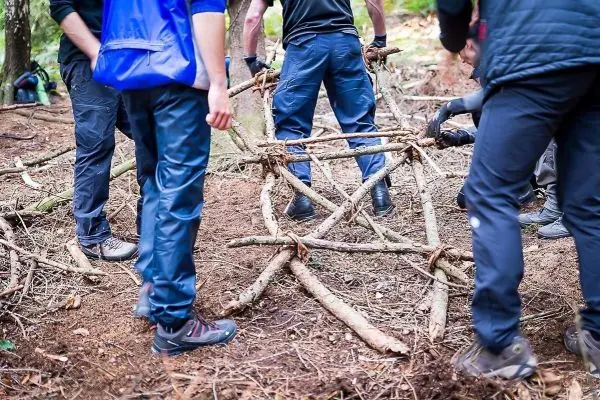 Gruppierung von Personen baut eine selbstgebaute Konstruktion aus Ästen im Wald