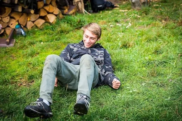 Junge sitzt auf dem Gras und lacht, Holzstapel im Hintergrund