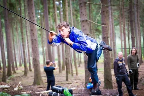 Junge überquert selbstgebaute Seilbrücke zwischen Bäumen im Wald