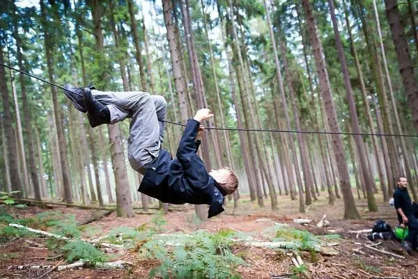 Junge überquert selbstgebaute Seilbrücke zwischen Bäumen im Wald