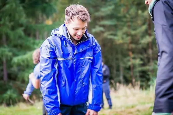 Junger Mann in blauer Regenjacke beugt sich nach vorne in einer Waldumgebung