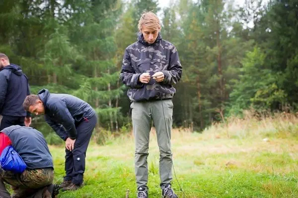 Junger Mann prüft Ausrüstung im Wald, während andere sich bücken
