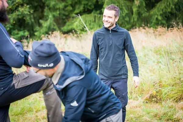 Lächelnder Mann steht in einer Wiese, während andere Personen aktiv sind