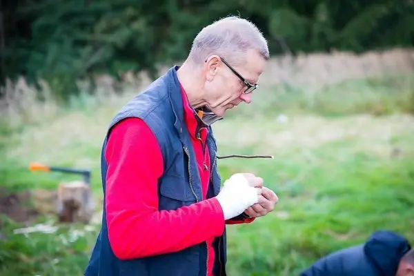 Mann hält einen Stock in der Hand und bearbeitet ihn mit einem Messer