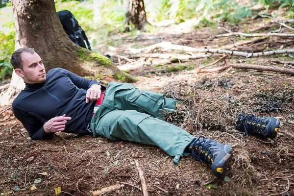 Mann liegt auf dem Boden im Wald und überprüft seine Ausrüstung