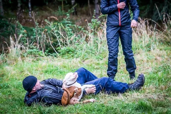 Mann liegt auf dem Boden und spielt mit einem Hund im Gras