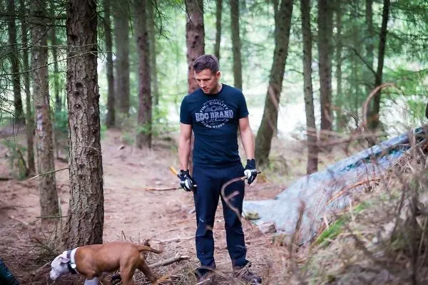 Mann mit Handschuhen steht im Wald neben einem Hund