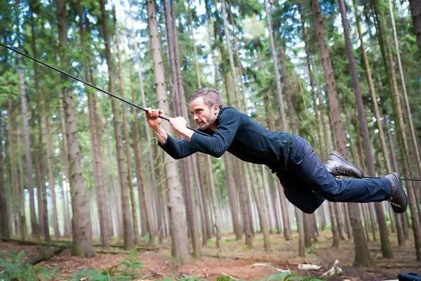 Mann überquert selbstgebaute Seilbrücke zwischen Bäumen im Wald