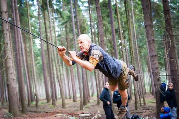 Mann überquert selbstgebaute Seilbrücke zwischen Bäumen im Wald