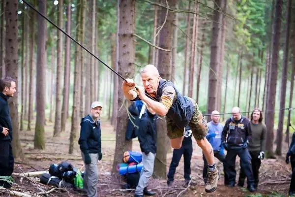 Mann überquert selbstgebaute Seilbrücke zwischen Bäumen im Wald