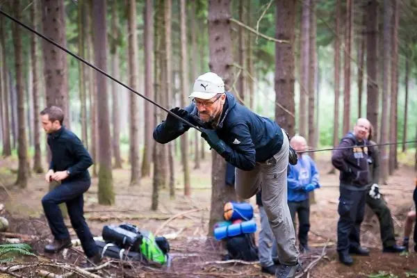 Mann überquert selbstgebaute Seilbrücke zwischen Bäumen im Wald