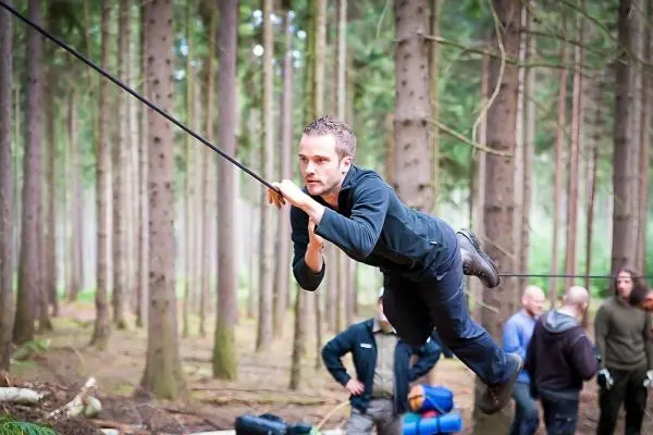 Mann überquert selbstgebaute Seilbrücke zwischen Bäumen im Wald