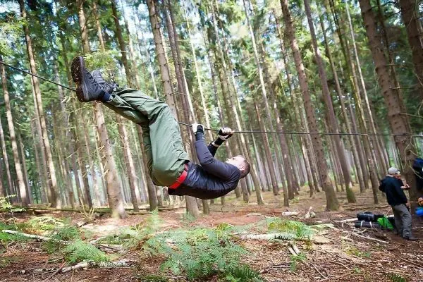Mann überquert selbstgebaute Seilbrücke zwischen Bäumen im Wald